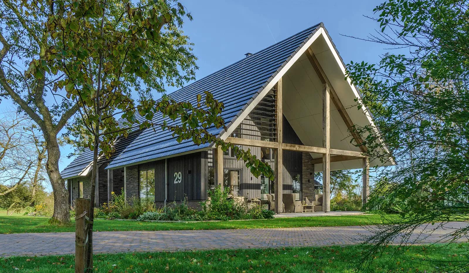 Schuurwoning in Steggerda met zwarte gevel, houten spanten, blauwe dakvloering en overkapping, omgeven door groen